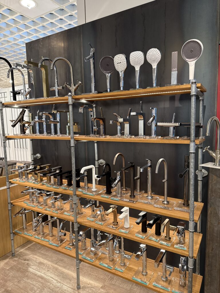 Armaturenwand in der Badausstellung: Dutzende Armaturen und Duschköpfe auf Holzbrettern montiert, zum Anfassen und Vergleichen
